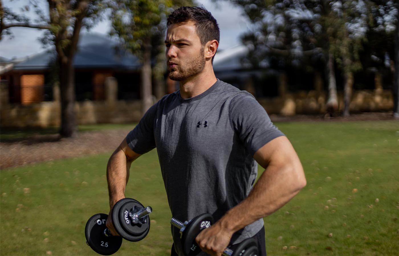 A male athlete performing free weight shoulder exercises with a pair of dumbbells